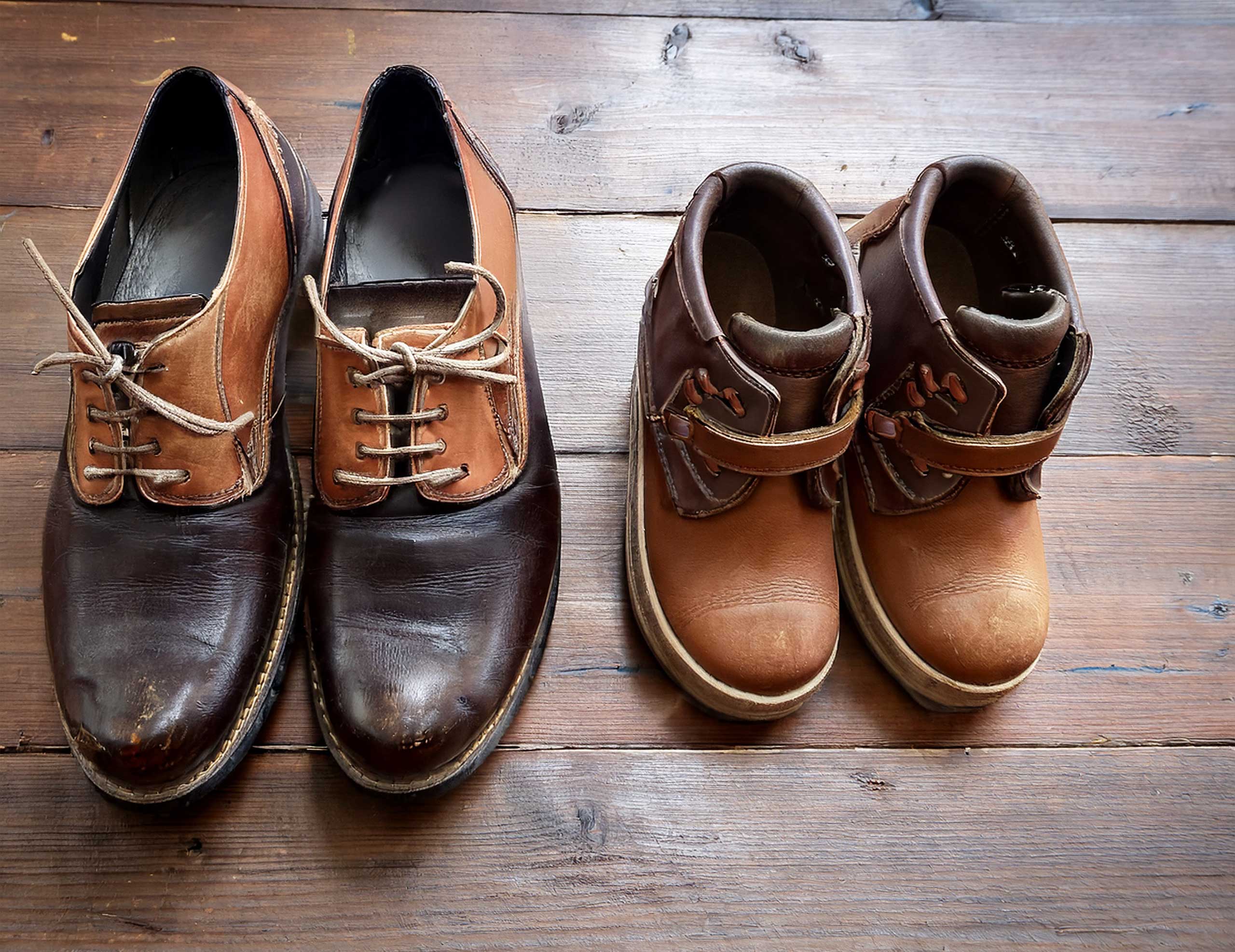A pair of well-worn men’s shoes beside a child’s pair on a wooden floor A pair of well-worn men’s shoes beside a child’s pair on a wooden floor
